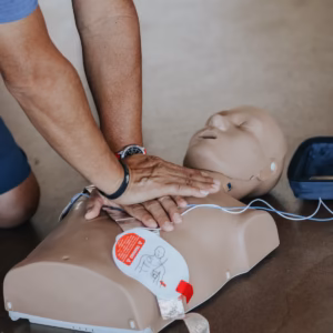 hands practising CPR on a training manikin with an AED nearby